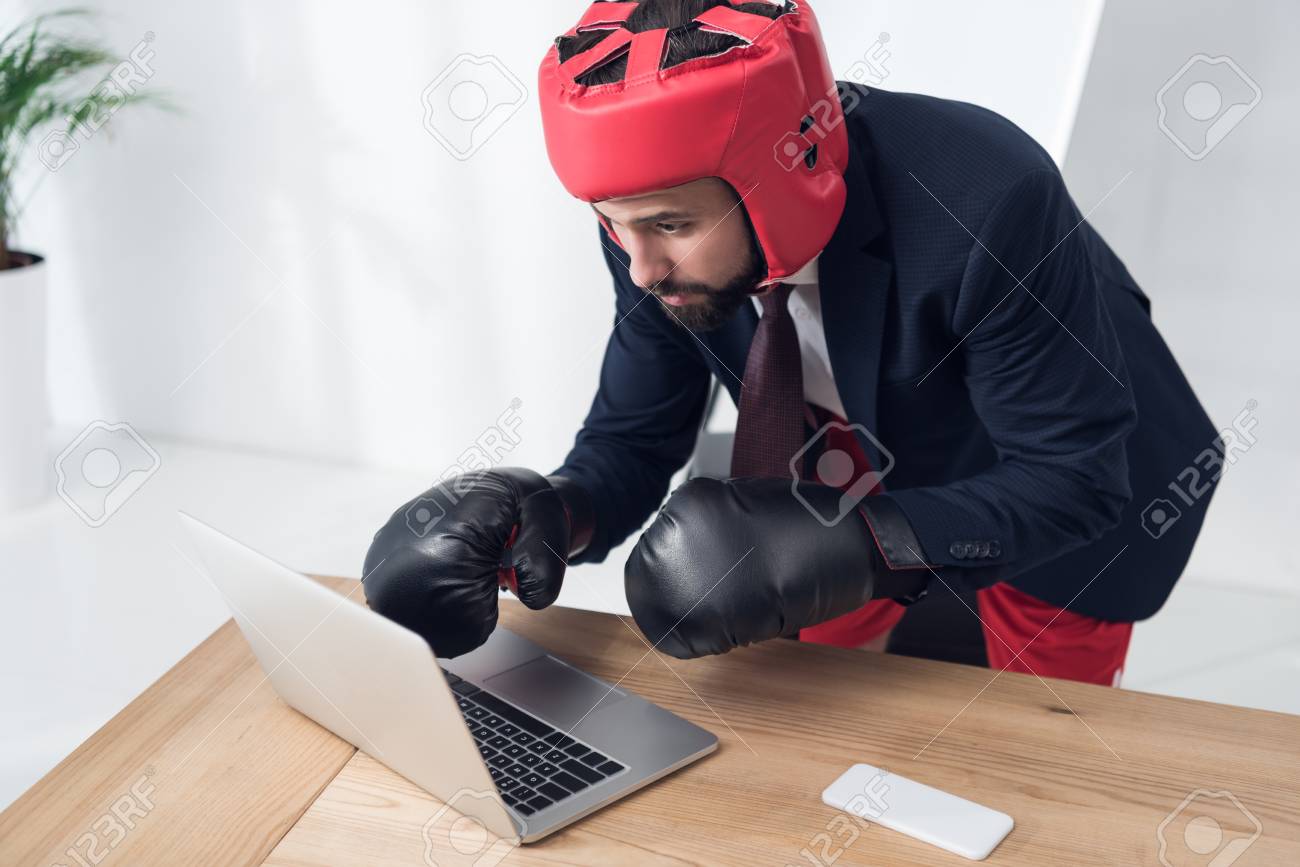 104564057-businessman-in-boxing-gloves-and-helmet-typing-on-laptop-at-workplace-in-office.jpg